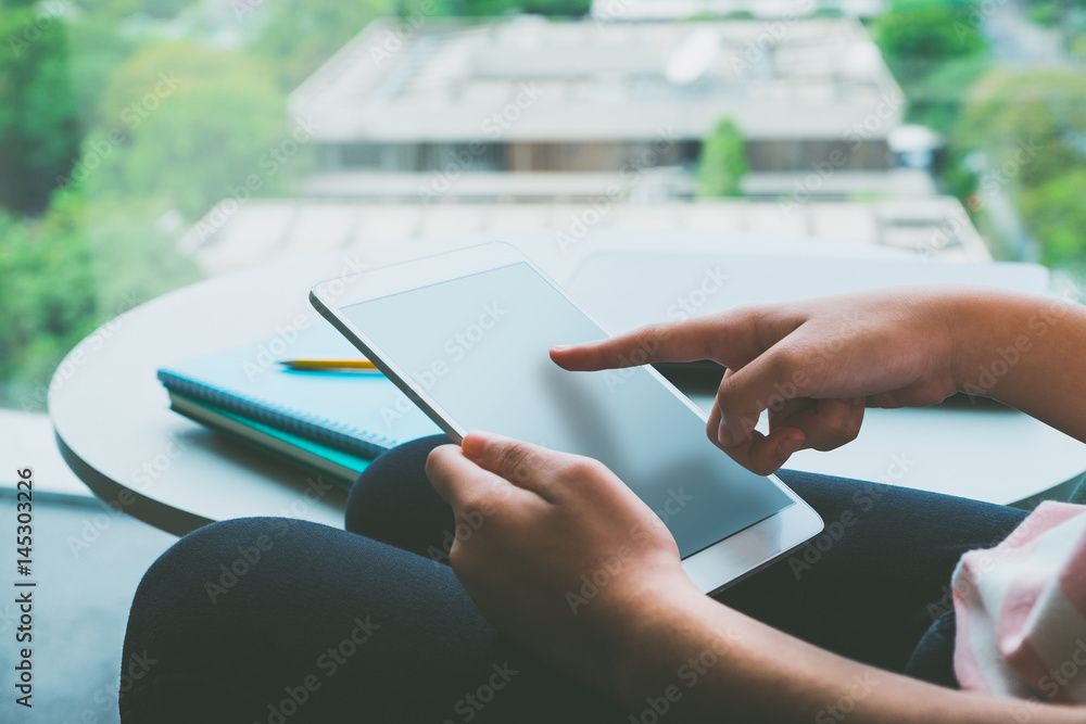 Poster Close up hand of woman sitting and touch blank screen of tablet computer with lecture notebook and pencil on table near campus window,Online education (e-learning) concept, Vintage filter
