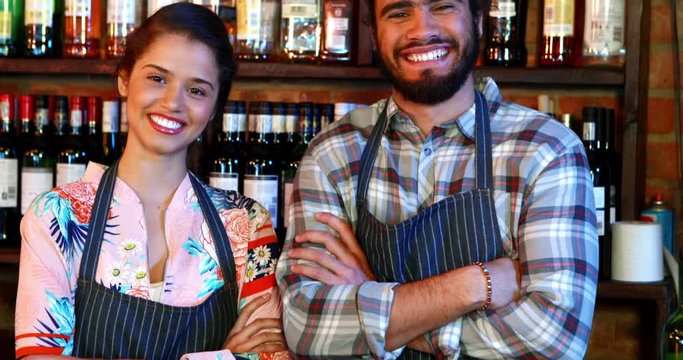 Portrait of barmaid and barman standing with arms crossed at bar counter