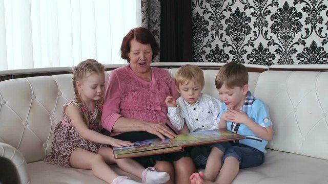 Old woman with her grandchildren looking at the photos in the photo album.
