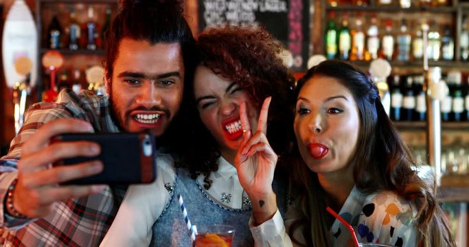 Friends taking selfie on mobile phone while having cocktail
