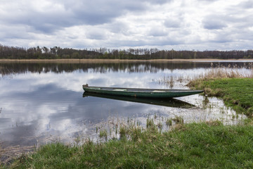 Fish pond in the spring in the middle of April. Fishing boat near the green shore. A  forest in the background. Podlasie, Poland.