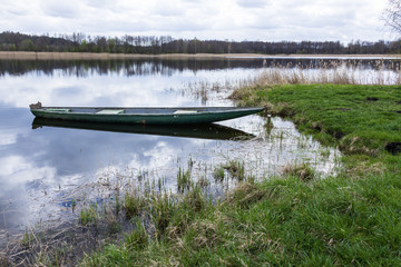 Fish pond in the spring in the middle of April. Fishing boat near the green shore. A  forest in the background. Podlasie, Poland.