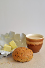 Breakfast of one bun with flax seeds, pieces of butter, cup of beverage with copy space