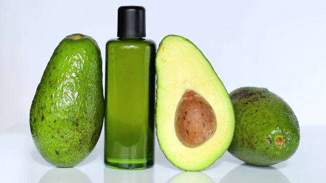 Avocado oil in a green glass bottle, avocado in a cut on a white background