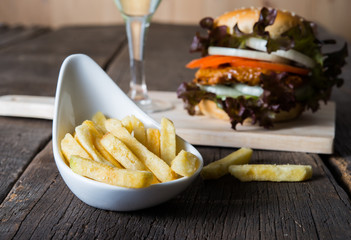Close up of french fries with Homemade chicken burger, lettuce, tomato and onion on wooden board.
