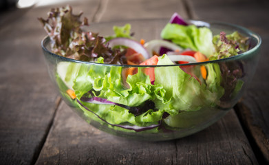 Fresh vegetable salad in glass bowl on wooden background.