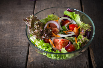 Fresh vegetable salad in glass bowl on wooden background.