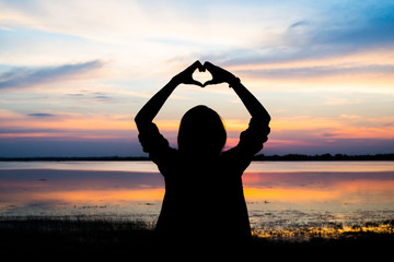 Silhouette of woman hands in heart shape with sunrise in the middle and beach background