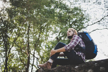 Young hipster man sitting on a tree branch in the park.