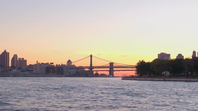 ESTABLISHING SHOT: Silhouette of iconic Manhattan bridge and Brooklyn bridge at golden sunset with Downtown Manhattan NYC skyline in the background. Beautiful view of New York City cityscape at sunset