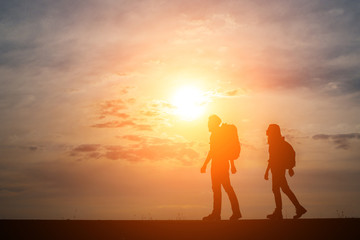 Silhouettes of two hikers with backpacks enjoying sunset. Travel concept.