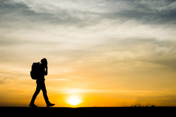 Silhouette of the young backpacker man walking  during sunset.