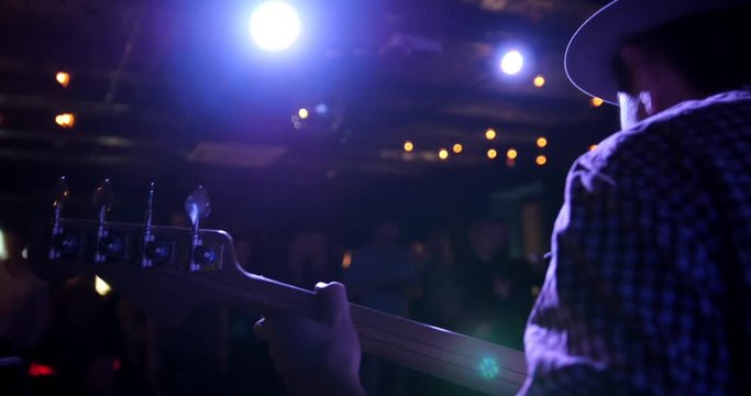 Musician - guitarist in hat plays guitar in night club, rear view