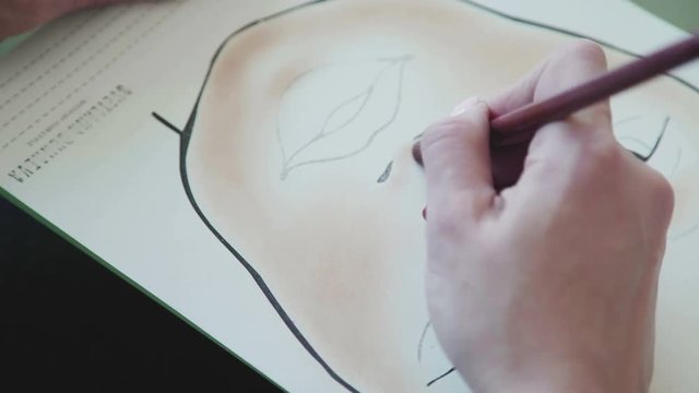 Young woman in a bright studio draws a facechart. The make-up artist draws a schematic image of a face on watercolor paper and applies make-up. Make-up artist learns to apply make-up using face map