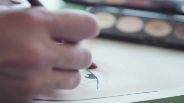 Make-up artist creates a make-up sketch on the face chart. Face chart of cosmetic brand. Inspiration: the make-up artist draws face-lines on watercolor paper, using professional cosmetics.