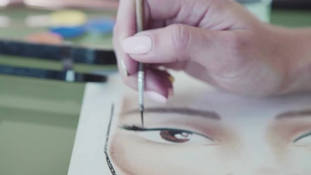 Make-up artist creates a make-up sketch. Young woman in a bright studio draws a facechart. Face sculpting - training on the face-chart. Close-up: artist paints a portrait and focuses on the eyelashes