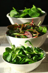 Three white bowls of fresh salads on wooden background. Baby spinach, mesclun and mache.