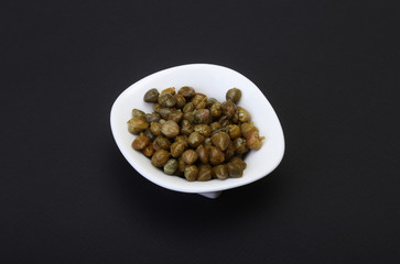 bowl with fresh capers isolated on black background.