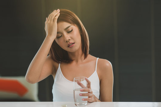Beautiful young Asian woman taking pill against headache at home.(Soft photo)