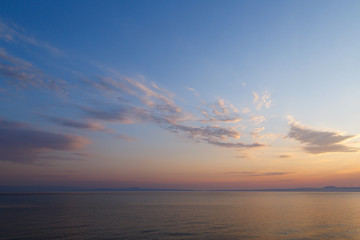 Early morning at dawn of the day with a calm blue sea overlooking the cloudy sky and mountains of the other shore