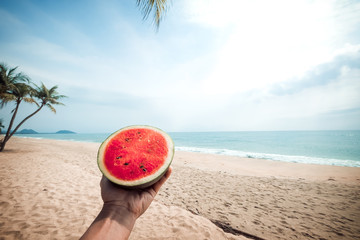 Relaxation and Leisure - Lifestyle image of hand holding a watermelon. Tropical island beach. Summer vacation concept. vintage color tone.