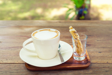Coffee cup and pastry on wooden table with nature background.
