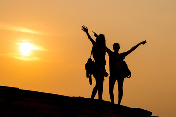 Silhouette of cheering young happy couple raising their arms to sunrise at sea
