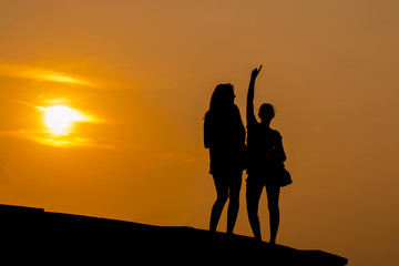 Silhouette of cheering young happy couple raising their arms to sunrise at sea