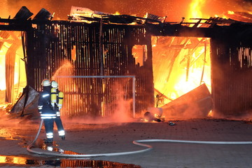 Großbrand einer Halle mit heftigem Feuer und Löscharbeiten der Feuerwehr.