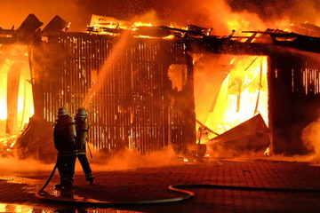 Naklejka premium Großbrand einer Halle mit heftigem Feuer und Löscharbeiten der Feuerwehr.