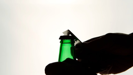 Silhouette of Male hands opening brown beer bottle with opener