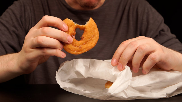 Young adult eats a doughnuts from a papper bag