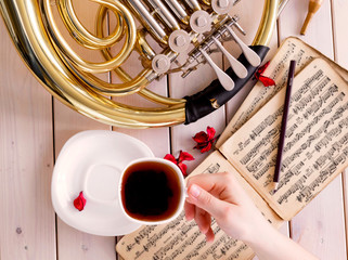 French horn on light wooden background. Musical background – French horn, tea, notes.