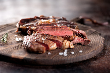 Ribeye steak slices with salt and rosemary on a wooden serving board