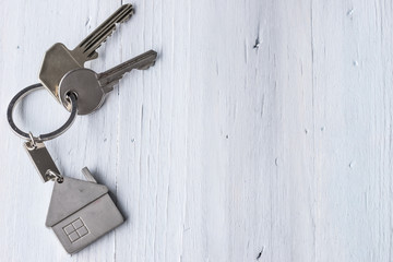 House key on a house shaped keychain on wooden floorboards or wooden table.
