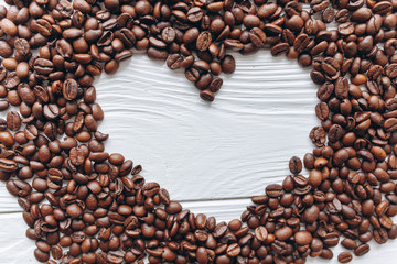 Heart of coffee beans on white wooden background