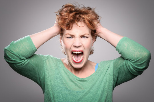 Middle aged, mature, attractive woman screaming covering her ears. 