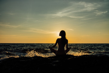 Silhouette meditation girl lotus position on stone on the background of the stunning sea.