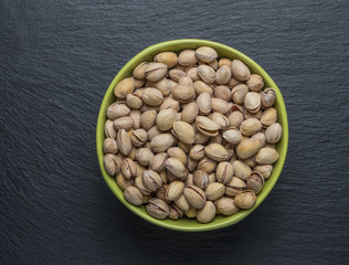 Pistachio nuts in a green plate on a dark background