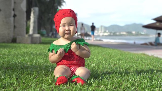 Close-up Asian baby girl wearing strawberry costume eat cookies on the beach.