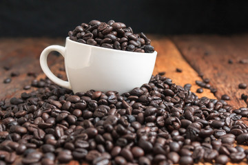 Fototapeta premium Close up shot of dark roasted coffee bean in white ceramic cup on wooden floor with copy space