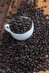 Close up shot of dark roasted coffee bean in white ceramic cup on wooden floor with copy space