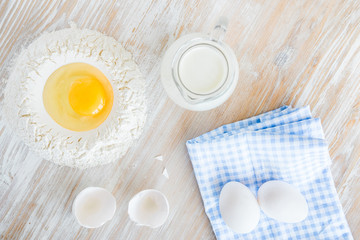 Ingredients and tools for baking - flour, eggs and glass of milk on the wooden rustic table background, selective focus