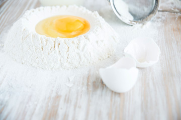 Ingredients and tools for baking - flour, eggs and glass of milk on the wooden rustic table background, selective focus