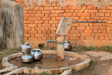 Old hand operated water pump and water containers in rural India.
