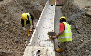 Construction workers installing precast u-shape concrete drain at the construction site. The drain was fabricated at factory and mobilized to site.  © Aisyaqilumar