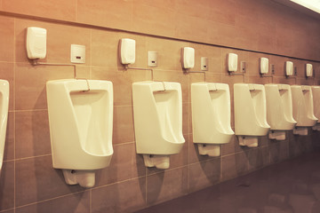 Row of white urinal for men on tile wall in toilet.