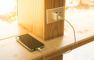 Mobile phone charger plugged on  wooden pole in the coffee shop with sunlight in morning time.