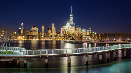 Fototapeta na wymiar New York City Financial District skyscrapers and Hudson River from Hoboken promenade in evening. Lower Manhattan skyline and pedestrian bridge from New Jersey