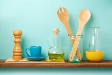Kitchen shelf with utensils, salt, oil bottle and cup over blue background